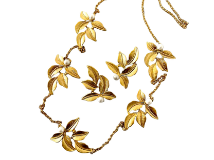 a gold necklace with flowers and pearls on a black background